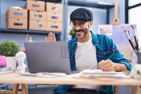 Photo for Hispanic man with beard doing online video call at art studio looking positive and happy standing and smiling with a confident smile showing teeth - Royalty Free Image