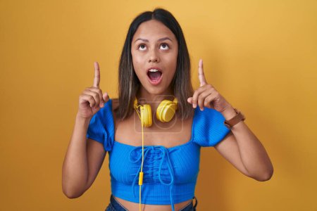 Téléchargez les photos : Hispanic young woman standing over yellow background amazed and surprised looking up and pointing with fingers and raised arms. - en image libre de droit