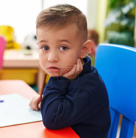 Foto de Adorable hispanic boy preschool student sitting on table drawing on paper at kindergarten - Imagen libre de derechos