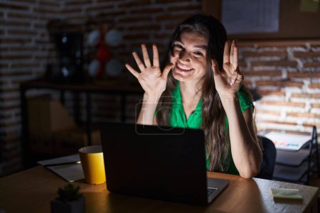 Foto de Joven adolescente que trabaja en la oficina por la noche mostrando y apuntando hacia arriba con los dedos número nueve mientras sonríe confiado y feliz. - Imagen libre de derechos