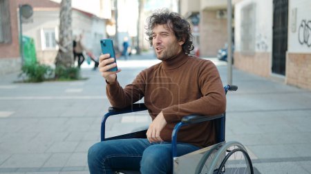 Téléchargez les photos : Young hispanic man having video cal sitting on wheelchair at street - en image libre de droit