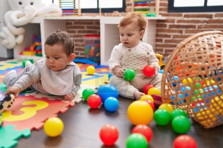 Foto de Dos adorables bebés jugando con bolas sentados en el suelo en el jardín de infantes - Imagen libre de derechos