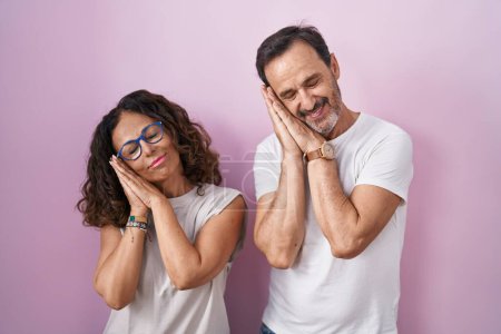 Téléchargez les photos : Middle age hispanic couple together over pink background sleeping tired dreaming and posing with hands together while smiling with closed eyes. - en image libre de droit