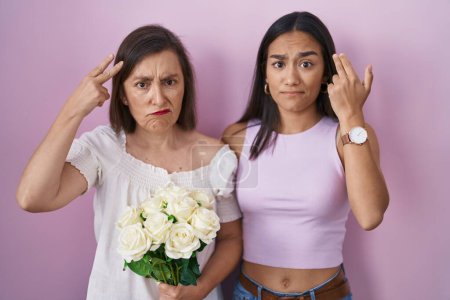 Photo for Hispanic mother and daughter holding bouquet of white flowers shooting and killing oneself pointing hand and fingers to head like gun, suicide gesture. - Royalty Free Image