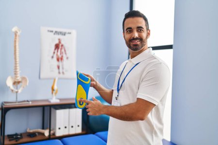 Photo for Young hispanic man podiatrist holding insole at podiatry center - Royalty Free Image
