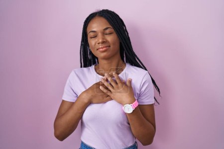 Photo for African american woman with braids standing over pink background smiling with hands on chest with closed eyes and grateful gesture on face. health concept. - Royalty Free Image