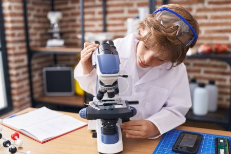 Téléchargez les photos : Adorable étudiant garçon caucasien utilisant le microscope en classe - en image libre de droit