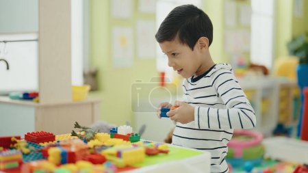 Photo for Adorable hispanic boy playing with construction blocks sitting on table at kindergarten - Royalty Free Image