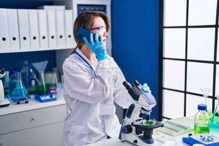 Téléchargez les photos : Jeune femme scientifique utilisant le microscope parlant sur smartphone au laboratoire - en image libre de droit