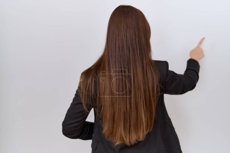 Photo for Beautiful brunette woman wearing business jacket and glasses posing backwards pointing ahead with finger hand - Royalty Free Image