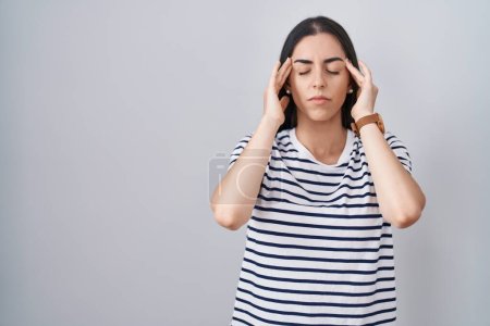 Junge brünette Frau in gestreiftem T-Shirt mit der Hand auf dem Kopf, Kopfschmerzen wegen Stress. Migräne. 