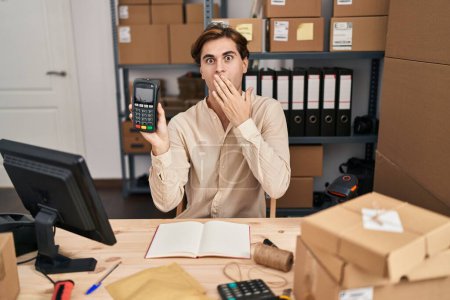 Photo for Young man working at small business ecommerce holding dataphone covering mouth with hand, shocked and afraid for mistake. surprised expression - Royalty Free Image