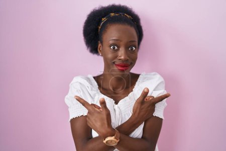 Téléchargez les photos : African woman with curly hair standing over pink background pointing to both sides with fingers, different direction disagree - en image libre de droit
