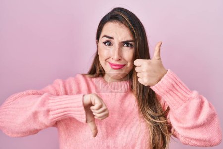 Téléchargez les photos : Young hispanic woman standing over pink background doing thumbs up and down, disagreement and agreement expression. crazy conflict - en image libre de droit
