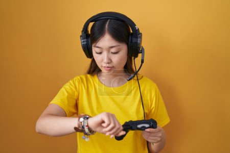 Photo for Chinese young woman playing video game holding controller checking the time on wrist watch, relaxed and confident - Royalty Free Image