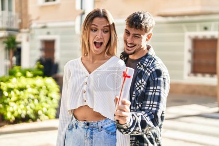 Téléchargez les photos : Jeune homme et femme couple souriant confiance debout tenant cadeau à la rue - en image libre de droit