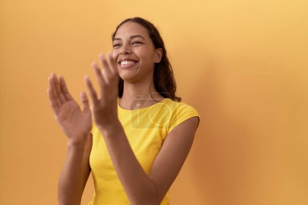 Téléchargez les photos : Jeune femme afro-américaine souriante applaudissements confiants applaudissements sur fond jaune isolé - en image libre de droit