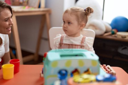 Téléchargez les photos : Professeur et tout-petit assis sur la table jouant avec des jouets à la maternelle - en image libre de droit