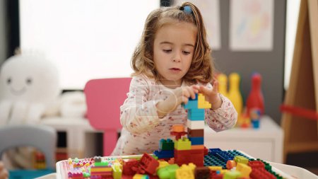 Foto de Adorable chica hispana jugando con bloques de construcción sentada en la mesa en el jardín de infantes - Imagen libre de derechos