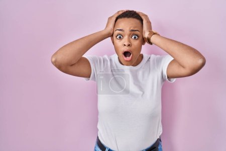 Photo for Beautiful african american woman standing over pink background crazy and scared with hands on head, afraid and surprised of shock with open mouth - Royalty Free Image