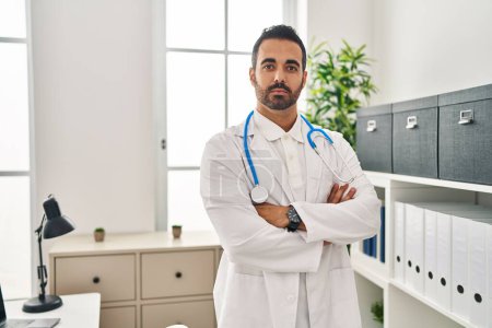 Téléchargez les photos : Young hispanic man wearing doctor uniform standing with arms crossed gesture at clinic - en image libre de droit