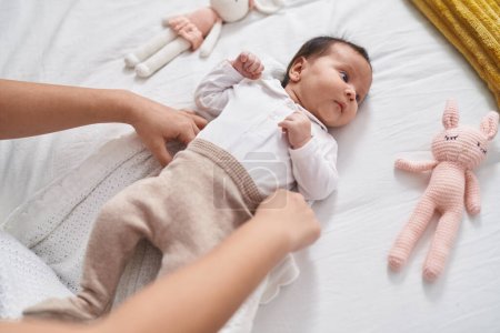 Téléchargez les photos : Adorable bébé hispanique portant des vêtements allongés sur le lit dans la chambre - en image libre de droit