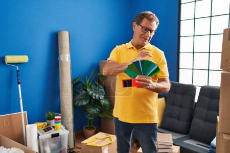 Téléchargez les photos : Middle age man smiing confident choosing paint color wall at new home - en image libre de droit