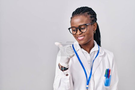 Photo for African woman with braids wearing scientist uniform pointing thumb up to the side smiling happy with open mouth - Royalty Free Image