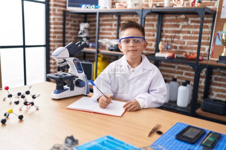 Téléchargez les photos : Adorable élève hispanique garçon utilisant l'écriture au microscope sur ordinateur portable à la salle de classe de laboratoire - en image libre de droit