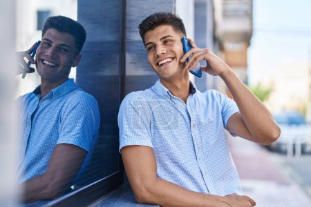Foto de Joven hombre hispano sonriendo confiado hablando en el teléfono inteligente en la calle - Imagen libre de derechos