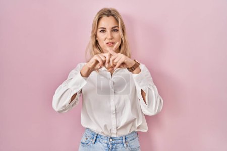 Téléchargez les photos : Jeune femme caucasienne portant une chemise blanche décontractée sur fond rose expression de rejet croisant les doigts faisant signe négatif - en image libre de droit
