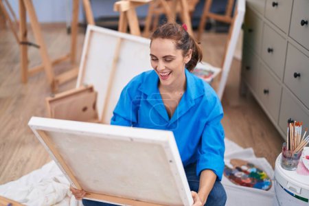 Téléchargez les photos : Jeune femme artiste regardant dessiner assis sur le sol à l'atelier d'art - en image libre de droit