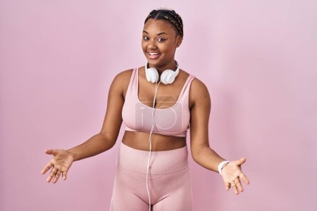 Téléchargez les photos : African american woman with braids wearing sportswear and headphones smiling cheerful with open arms as friendly welcome, positive and confident greetings - en image libre de droit