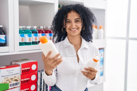 Foto de Young hispanic woman customer smiling confident choosing sunscreen lotion at pharmacy - Imagen libre de derechos