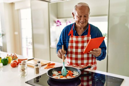 Téléchargez les photos : Senior homme souriant cuisine confiante et regarder la recette en ligne à la cuisine - en image libre de droit