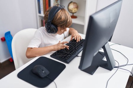 Foto de Adorable estudiante chico caucásico usando computadora sentada en la mesa en el aula - Imagen libre de derechos