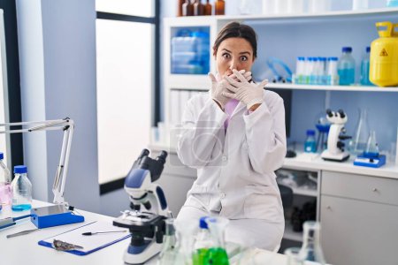 Téléchargez les photos : Young brunette woman working at scientist laboratory shocked covering mouth with hands for mistake. secret concept. - en image libre de droit
