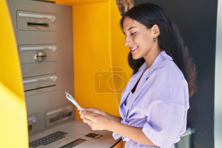 Photo for Young beautiful hispanic woman smiling confident holding dollars on bank teller at street - Royalty Free Image
