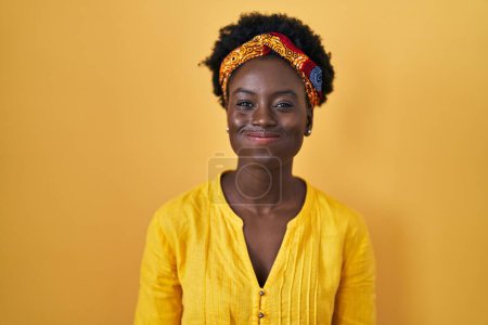 Foto de Mujer joven africana con turbante africano soplando mejillas con cara divertida. boca hinchada de aire, expresión loca. - Imagen libre de derechos