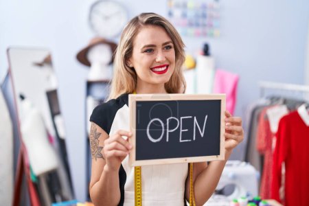 Photo for Young beautiful hispanic woman tailor smiling confident holding open blackboard at clothing factory - Royalty Free Image
