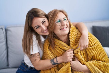 Foto de Madre e hija abrazándose sentadas en el sofá en casa - Imagen libre de derechos