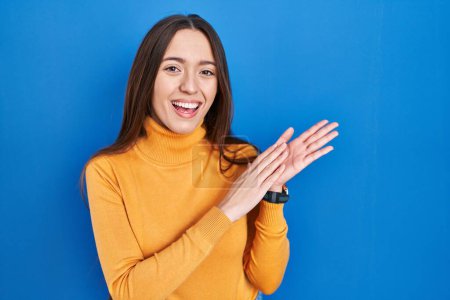 Téléchargez les photos : Jeune femme brune debout sur fond bleu applaudissant et applaudissant heureux et joyeux, souriant mains fiers ensemble - en image libre de droit