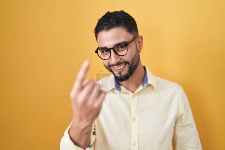 Foto de Hispanic young man wearing business clothes and glasses beckoning come here gesture with hand inviting welcoming happy and smiling - Imagen libre de derechos