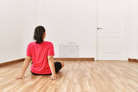 Photo for Young beautiful hispanic woman sitting on floor on back view at empty room - Royalty Free Image