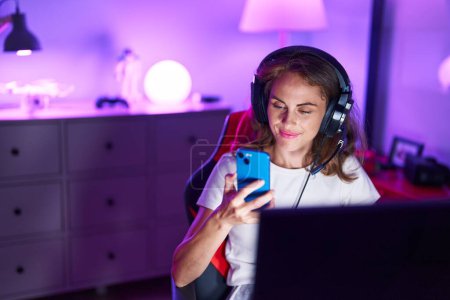 Téléchargez les photos : Jeune belle hispanique femme streamer en utilisant l'ordinateur et le smartphone à la salle de jeux - en image libre de droit