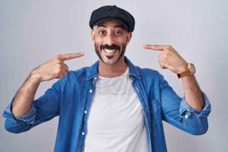Téléchargez les photos : Homme hispanique avec la barbe debout sur fond isolé souriant gai montrant et pointant avec les doigts dents et la bouche. concept de santé dentaire. - en image libre de droit