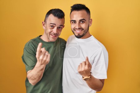 Photo for Homosexual couple standing over yellow background beckoning come here gesture with hand inviting welcoming happy and smiling - Royalty Free Image