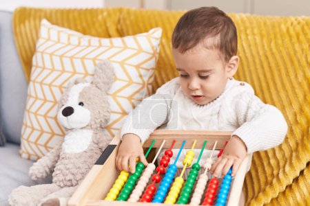 Photo for Adorable hispanic toddler playing with abacus sitting on sofa at home - Royalty Free Image