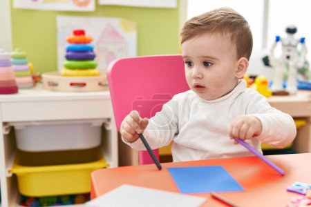 Téléchargez les photos : Adorable caucasien bébé étudiant assis sur la table dessin sur papier à la maternelle - en image libre de droit