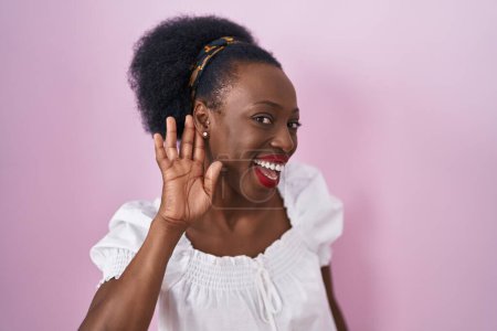 Téléchargez les photos : African woman with curly hair standing over pink background smiling with hand over ear listening an hearing to rumor or gossip. deafness concept. - en image libre de droit